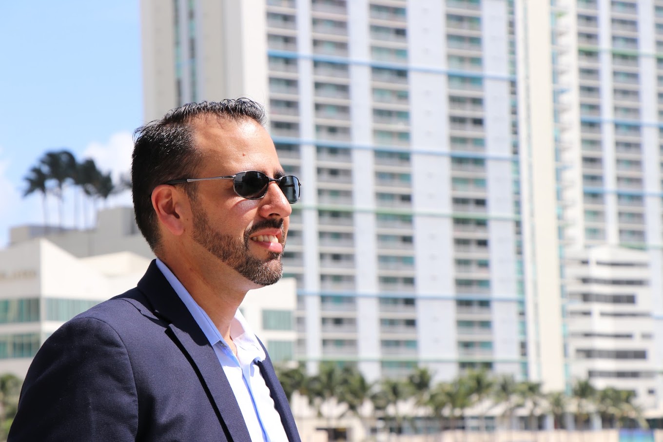 Una persona con saco y lentes de sol, al aire libre frente a edificios de la ciudad, durante una sesión fotográfica corporativa de Safeguard and Associates.