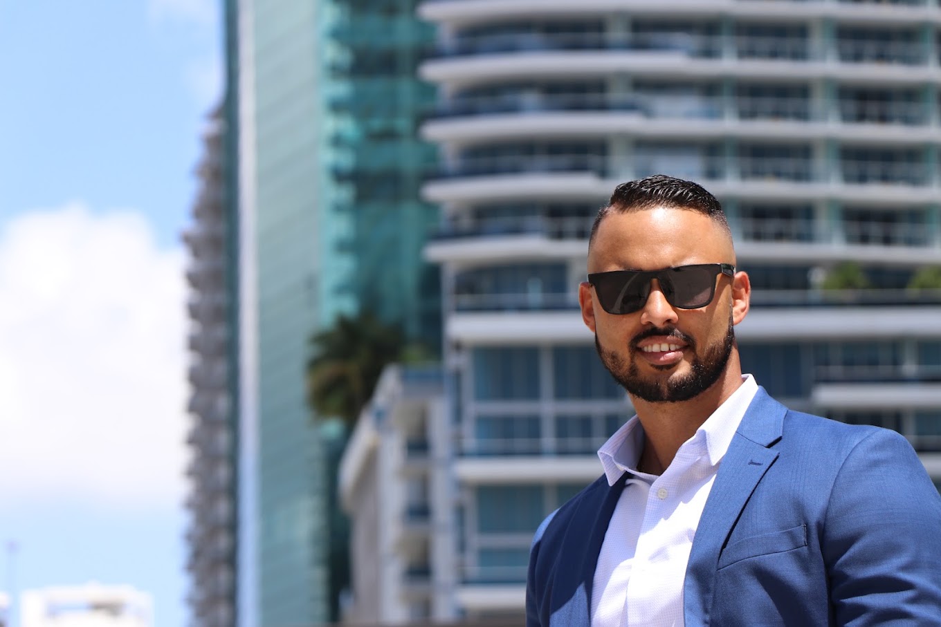 Una persona con saco azul y lentes de sol, al aire libre frente a edificios altos, durante una sesión fotográfica corporativa de Safeguard and Associates.
